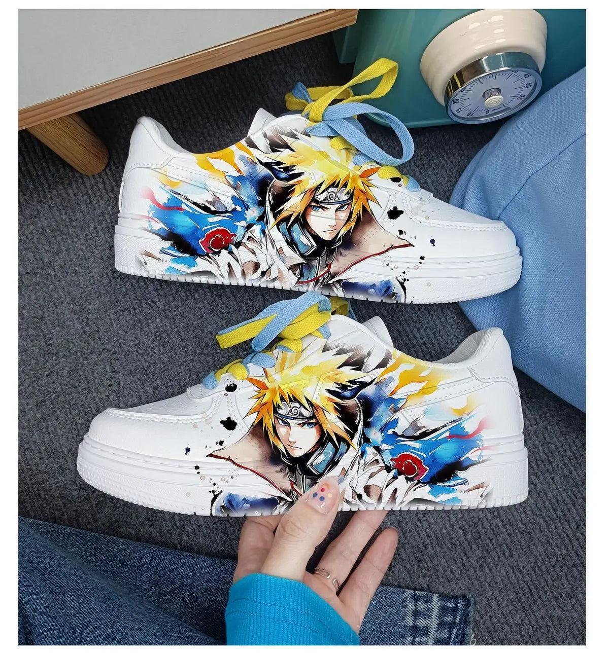 Pair of white Naruto Minato low-top sneakers held in hand, showing Minato artwork with red cloud accents